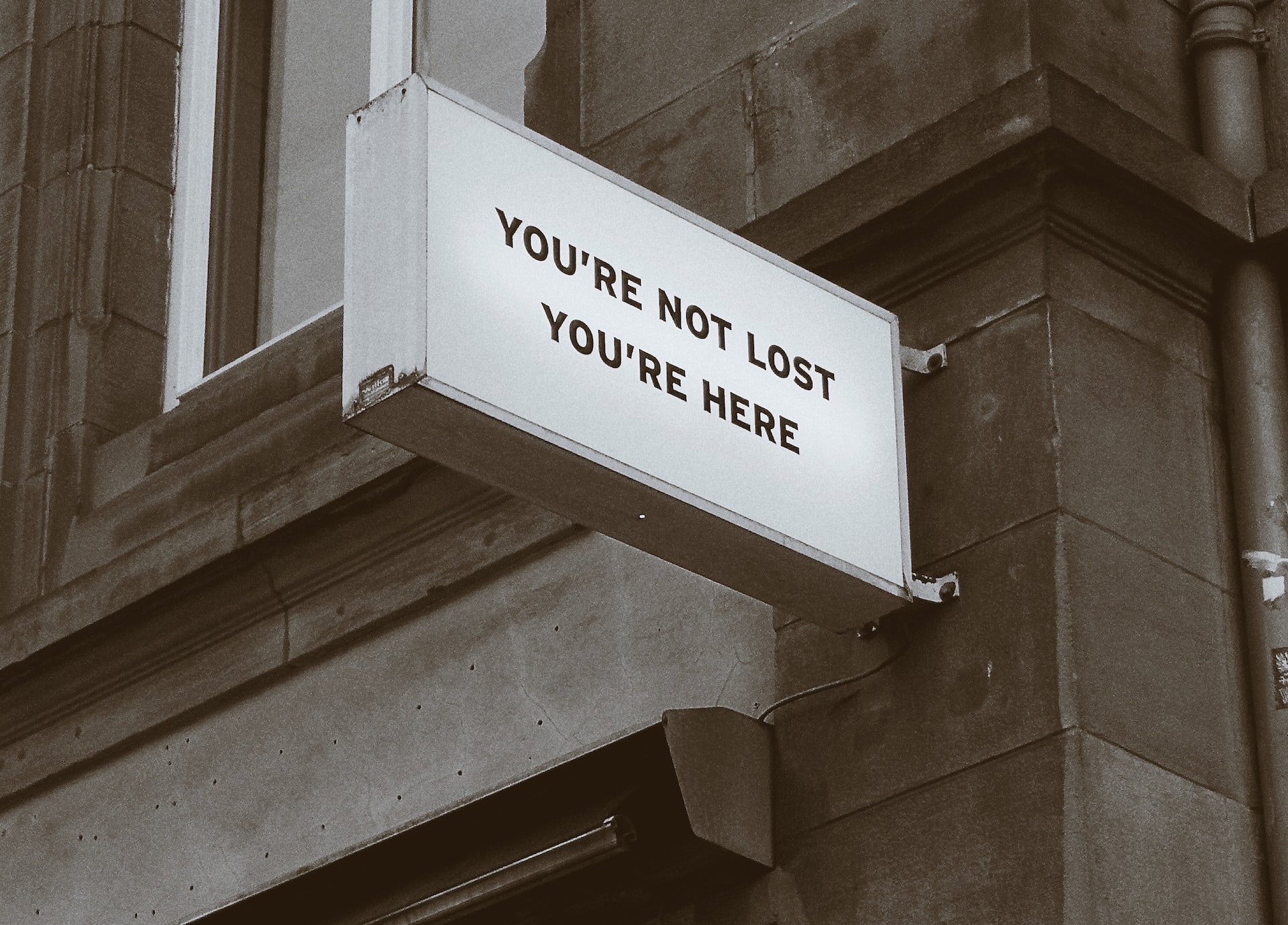 Abstehendes Schild an Hauswand mit der Aufschrift: You're not lost you're here